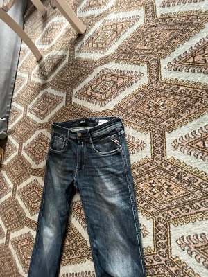 Replay jeans - Säljer ett par blå jeans från Replay, modell ANBASS, i storlek W32 L32. Jeansen har en klassisk rak passform och subtila slitningar som ger en avslappnad men stilren känsla. Tillverkade i kvalitetsdenim med fem fickor och en design som aldrig går ur tiden. Perfekta jeans till både vardag och mer uppklädda tillfällen.