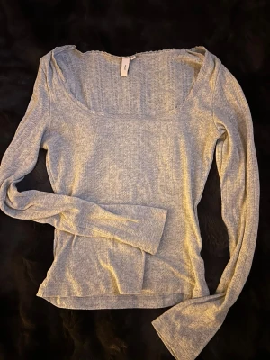 Ljusgrå långärmad topp från Nelly - Säljer en ljusgrå långärmad topp från Nelly med ribbad struktur och små hålmönster. Toppen har en bred, rundad halsringning med spetskant