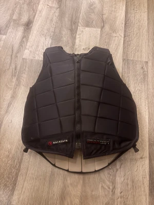 Svart säkerhetsväst från Racesafe - Säljer en svart säkerhetsväst från Racesafe, storlek Childs Large.  Den är i bra skick har nån fläck men går bort om man tvättar med vatten 