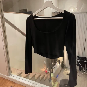 Svart croppad långärmad topp - Säljer en svart croppad topp med lång ärm och djup rundad halsringning. Enkel och stilren design som passar till många olika outfits. Materialet känns mjukt och stretchigt mot huden.