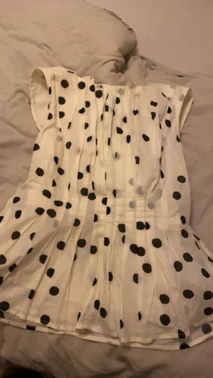 Vit prickig blus från Vero Moda - Säljer en vit blus från Vero Moda i storlek M med svarta prickar. Blusen har korta ärmar, rund hals och dragkedja i sidan. Materialet är lätt och luftigt, perfekt för vår och sommar. Den har ett snyggt veckat fall som ger en cool och feminin vibe.