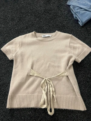 Beige stickad topp med knyt från Zara - Säljer denna eftertraktade tröja från Zara. Använd fåtal gånger, är som ny. Jättefin men kommer inte till användning