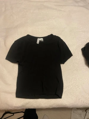 Svart ribbad t-shirt magtröja  - Säljer en svart ribbad t-shirt från Cropp med korta ärmar och rund hals. T-shirten har en enkel och clean look, perfekt för att matcha med jeans eller shorts. Materialet är mjukt och stretchigt bomull som sitter skönt mot kroppen.