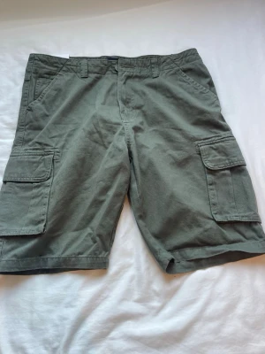 Gröna helt nya cargo shorts  - Säljer ett par HELT NYA MED PRISLAPP, gröna cargo shorts från Lager 157 med flera praktiska fickor på sidorna och bak. Perfekta för chill dagar och har klassiska bälteshällor och knappstängning framtill. Storlek M