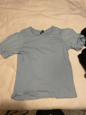 Ljusblå blus med broderade puffärmar - Supersöt ljusblå blus från veromoda med puffiga kortärmar i broderad bomull. Ärmarna har fina hålbroderier och ger en romantisk vibe. Perfekt till jeans eller kjol för en fräsch look.