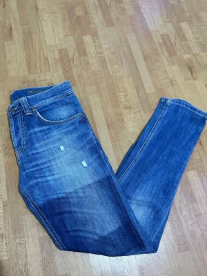 Dondup Mius - Säljer ett par blå jeans från Dondup med klassisk femficksdesign och snygga slitningar på både fram- och baksida. Jeansen har slim fit och kontrastsömmar, samt Dondup-logga på bakfickan. Perfekt för dig som gillar en avslappnad stil.