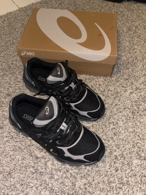 Asics Gel Nyc Graphite Grey/Black - Säljer ett par snygga Asics Gel Nyc sneakers i svart och grått med coola detaljer och logga på sidan. Skorna har snörning, rund tå och en platt sula. Ovandelen är i mesh och syntet för bra komfort och andning. Perfekt för dig som gillar sportig stil. Använda en gång. Inga tecken på slitage eller något liknande. Box kan fås med. Storlek 44,5 men då dom är små i storleken rekommenderar jag dessa till någon med runt 43 i storlek.