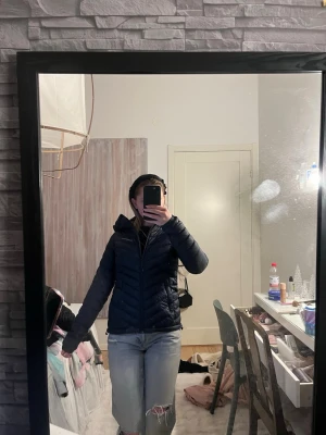 Mörkblå pufferjacka med huva - Säljer en mörkblå pufferjacka från Peak Performance. Jackan har en snygg, figurnära passform och är quiltad med dragkedja framtill. Utrustad med huva och två sidofickor. Perfekt för kyliga dagar och enkel att matcha med olika outfits.