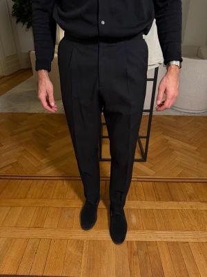 Svarta kostymbyxor från Suitsupply – 4-Ply Lanificio Rogna – Strl W30/L30 (utgångspunkt 48) - Säljer exklusiva svarta kostymbyxor från Suitsupply i 4-ply-tyg från Lanificio Rogna, känt för sin tyngd, hållbarhet och eleganta struktur. Sidospännen och stilrent uppslag. Ursprungligen stl 48, lätt insydd i midjan, motsvarar ca W30/L30. Ca 3 cm uttagna från knä och nedåt för rakare fall. Lätt tapered, nära rak modell. Endast kemtvättade, varsamt använda och i nära nyskick. Jag är 177 cm på bilderna. Paketpris vid flera köp.