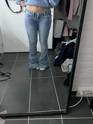 True Religion ljusblå bootcut jeans - Säljer ett par ljusblå jeans från True Religion med klassiska fickdetaljer och synliga sömmar. Modellen är lågmidjad med bootcut-ben som ger en schysst siluett. Jeansen har dragkedja och knapp framtill samt fickor med lock bak.