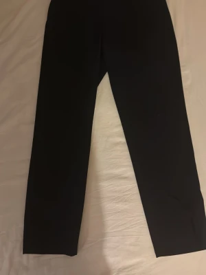 Svarta raka kostymbyxor - Snygga svarta kostymbyxor med rak passform och klassisk design. Perfekta för dig som gillar stilrena och enkla plagg. Byxorna har midwaist och är gjorda i ett slätt material som ger en clean look. Passar till många olika outfits och är ett måste i garderoben.