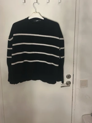 Svart stickad tröja med vita ränder Bikbok - Svart stickad tröja från Bikbok i storlek S. Tröjan har vita horisontella ränder och rund hals med ribbad kant. Långärmad och loose passform, perfekt för att chilla eller hänga med kompisar. Enkel och stilren design som funkar till jeans eller kjol. 