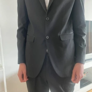 Svart kostym med skjorta, fluga och kostymbyxor  - Elegant svart kostym med kavaj, kostymbyxor, 2 skjortor, och fluga. Perfekt för studenten.  Bara använd 1 gång köpte för 4000 men säljer allt för 200, kan också sälja separat.  Kostymbyxa och kavaj- selected homme Fluga- pier one Vit skjorta-NEXT svart skjorta- jack & jones