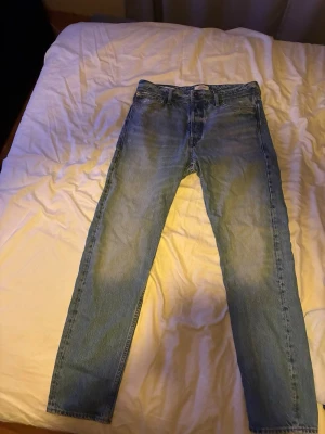 Blå loose fit jeans från Jack & Jones - Säljer ett par ljusblå loose fit jeans från Jack & Jones. Loose/chris modell. Klassisk femficksmodell med raka ben och normal midja. Jeansen har slitningar och en avslappnad look, perfekta för en chill stil. Materialet är tålig denim i bomull.