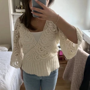 Vit omlott kofta med spetsdetaljer - Säljer en vit omlott tröja med breda trekvartsärmar och vackra spetsdetaljer. Koftan har ribbad nederkant och ett luftigt, stickat mönster som ger en bohemisk vibe. Perfekt att styla med jeans eller kjol för en chill look.
