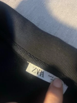 Zara quarter zip - Stilren och bekväm quarter zip-tröja i svart färg. Tillverkad i mjukt och tjockt material som passar perfekt för både vardag och skola. Dragkedja i halsen ger en modern look och gör den lätt att styla – snygg både öppen och stängd. Ribbad mudd nertill och vid ärmsluten för bra passform.  Skick: Mycket bra, inga hål eller fläckar. Passar perfekt till jeans, cargos eller mjukisbyxor.
