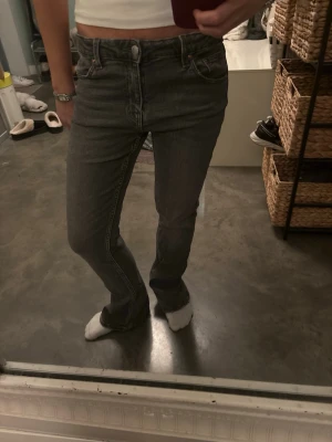 Bootcut grå jeans med mellan midja - Snygga bootcut jeans i mörkgrå tvätt med klassisk femficksdesign och hög midja. Jeansen har raka ben med lätt utsvängning nedtill och är tillverkade i ett mjukt denim-material. Perfekta för dig som gillar en retro vibe och vill ha en cool siluett.