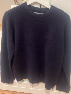 Mörkblå stickad tröja med rund hals - Säljer en enkel och stilren mörkblå stickad tröja med rundad hals och långa ärmar. Tröjan har en mjuk och lite fluffig yta, perfekt för kyliga dagar. Passar dig som gillar klassisk och avslappnad stil. Aldrig använd💕