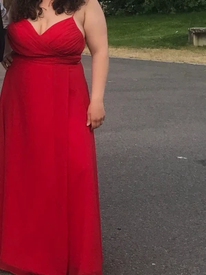 Röd långklänning med snörning - Säljer en röd långklänning med smala axelband och snygg snörning i ryggen. Klänningen har v-ringad omlottdesign upptill och ett flytande, elegant fall. Perfekt för bal eller student. Materialet känns lätt och följsamt. Jag är 157 och har på mig ca 10 cm klackar. Har använts en gång