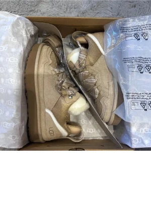 Beige UGG boots med snörning - Säljer ett par beige UGG boots med snörning och platt sula. Skorna har detaljer i vitt och insida med mjuk päls. Ovandelen är i mocka och textil, med grova snören och metallhål. Perfekta för kalla dagar och har en snygg, chunky look. Säljes pga fel storlek och bort tappat kvitto skickas imorgon pris kan diskuteras köptes för 2200 