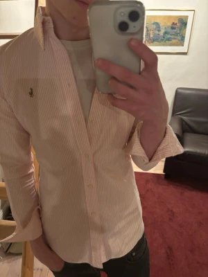 Rosa randig skjorta från Polo Ralph Lauren - Säljer en fräsch rosa och vit randig skjorta från Polo Ralph Lauren i storlek S, custom fit. Skjortan har knappt används och är i princip helt ny. Hör av er vid funderingar!
