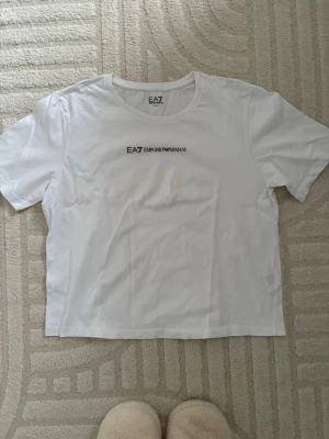 Vit EA7 Emporio Armani t-shirt S - Säljer en stilren vit t-shirt från EA7 Emporio Armani i storlek S. T-shirten har rund hals, korta ärmar och tryckt logga både fram och bak. Materialet är mjuk bomull som känns skönt mot huden. Perfekt för dig som gillar clean och enkel design.