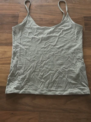 Beige linnetopp från Gina Tricot - Säljer en enkel och stilren beige/grön linnetopp från Gina Tricot, kollektionen Elevated Basics. Toppen har smala axelband och ärmlös design, perfekt för varma dagar. Materialet är mjukt och lätt bomull som känns skönt mot huden.