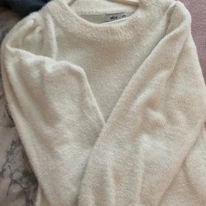 Vit fluffig stickad tröja från Ellos - Supermjuk och fluffig vit stickad tröja från Ellos i storlek 34/36. Tröjan har rund halsringning och långa ärmar, perfekt för kyliga dagar. 