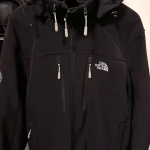 The North Face jacka - Svart vindjacka från The North Face med huva och flera dragkedjeförsedda fickor. Jackan har tekniskt material som står emot regn och kyla, samt vattenavvisande tyg. Luvan kan tas bort, likaså detaljerna på dragkedjorna om man vill förändra jackan lite kosmetiskt. En äventyrsjacka som klarar av allt när det kommer till väder och vind. Liten fläck på vänster arm som framgår på bilderna. 