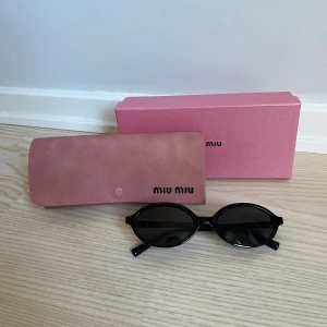 Svarta ovala solglasögon från Miu Miu - Snygga svarta solglasögon från Miu Miu med oval form och diskreta gulddetaljer vid gångjärnen. Kommer med original rosa fodral och ask.😊