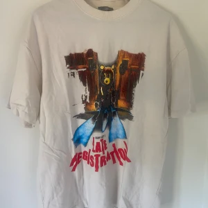 Kanye West Late Registration tour t-shirt - Vit t-shirt med tryck från Kanye Wests 'Late Registration' och 'Touch the Sky Tour 2005'. Framsidan har ikonisk björn-grafik och röd text, baksidan listar turnéstäder. Klassisk passform och rund hals. Perfekt för fans av hiphop och streetwear.