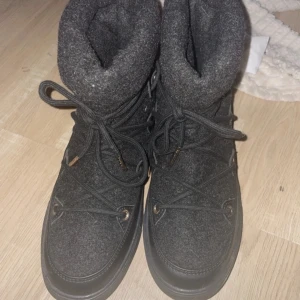 Svarta moon boots från Anna Field - Mysiga svarta nästan inukkis från Anna Field med snörning och detaljer i guld. Ovandel i filtliknande material och baksida i skinnimitation. Perfekta för kalla dagar med sin höga, vadderade design och platta sula.