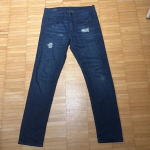 Mörkblå slitna jeans J.Lindeberg 31/32 - Mörkblå jeans från J.Lindeberg med snygga slitningar och trasiga detaljer framtill. Klassisk femficksmodell med raka ben. Perfektaför en avslappnad streetstil. Hör av er vid fingerringar. Priset kan diskuteras😁