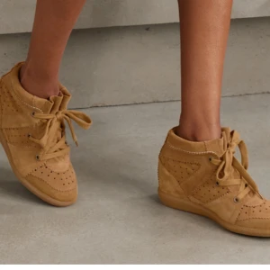 Bruna mockasneakers med snörning - Snygga sneakers i brun mocka med coola perforerade detaljer och bred snörning. Skorna har en rund tå och platt sula, samt en diskret kilklack för extra höjd. Perfekta för dig som gillar en avslappnad men trendig stil.