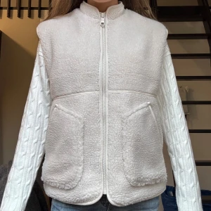 Off-white fleeceväst med dragkedja - Mysig vit fleeceväst med hög krage och två stora fickor framtill. Västen har en rak passform och stängs med dragkedja. Den är helt oanvänd (förutom när bilderna togs) och har etikettlappen kvar på sig originalpris 699kr!