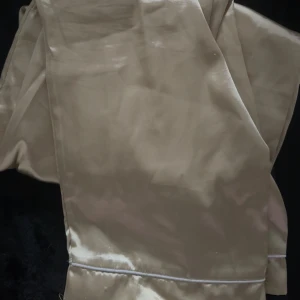 Beiga vida satinpants med resår - Snygga beiga byxor i glansigt satinmaterial med bred resår i midjan och vida ben. Byxorna har en avslappnad passform och en mjuk känsla, perfekta för en chill och trendig look.