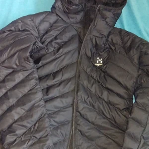 Svart pufferjacka från Haglöfs L - Säljer en svart pufferjacka från Haglöfs, modell Särna Mimic Hood. Jackan har huva, snygga diagonala quiltade paneler och dragkedja framtill. Perfekt för kalla dagar och har en clean look med diskret logga på bröstet.                                                        Mottog som födelsedagspresent men aldrig kommit till användning. Går att hämta i Örebro/skickas spårbart. 