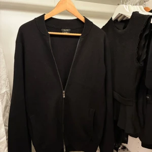 Svart ziptröja från Massimo Dutti - Stilren svart kofta från Massimo Dutti med dragkedja framtill och två fickor. Tillverkad i mjukt material med ribbade muddar vid hals och ärmslut. Perfekt för lager-på-lager och enkel att matcha med allt.