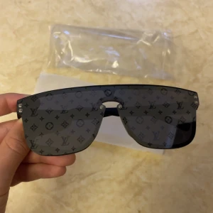 Svarta mongram glasögon - Snygga svarta solglasögon med monogrammönster på glasen. Modellen har en modern, rektangulär sköldform och mattsvarta bågar. Perfekt accessoar för dig som vill sticka ut med exklusiv stil.