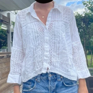 Vit spetsig skjorta med knappar - Säljer en vit skjorta med spetsdetaljer och knappar framtill. Skjortan har lång ärm och är tillverkad i ett lätt, luftigt material med broderade partier och hålmönster. Perfekt att matcha med jeans för en chill och fräsch look. Stolek L men passar mig som e en s