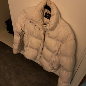 Beige pufferjacka - Säljer en beige pufferjacka i storlek XS. Jackan har hög krage, dragkedja och tryckknappar framtill. Den är vadderad och har en riktigt schysst oversized look som passar perfekt när det är kallt ute.