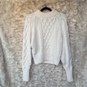 Vit stickad tjocktröja med flätmönster - Säljer en chunky vit/ cremefärgad stickad tröja med höga muddar och snyggt flätmönster både fram och på ärmarna. Tröjan har en hög, ribbad krage och är långärmad. Varm och skön.