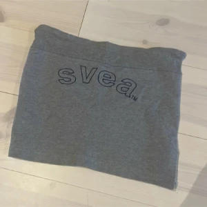 Grå kortkjol från Svea - Säljer en grå kortkjol från Svea med logga framtill. Kjolen är rak i modellen och har en liten slits på sidan. Tillverkad i mjukt bomullsmaterial som är skönt att bära. 