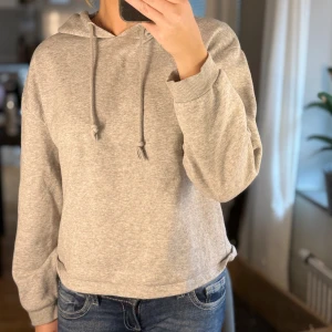 Grå hoodie med huva - Mysig grå hoodie i storlek L. Tröjan har huva med snörning och är tillverkad i mjuk bomullsblandning. Perfekt för chill dagar och enkel att matcha med jeans eller leggings. Klassisk passform och långa ärmar.