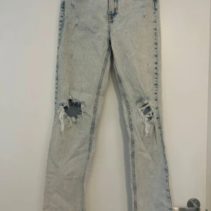 Ljusblå slitna bootcut jeans - Ljusblå jeans med bootcut passform och slitna hål över båda knäna. Jeansen har hög midja och klassisk femficksdesign. Materialet är denim i bomull och färgen är tvättad ljusblå. Perfekta för en avslappnad och trendig look.