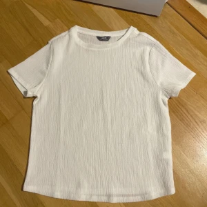 Vit ribbad t-shirt från Max - Vit t-shirt från Max med ribbad struktur och klassisk rund hals. T-shirten har korta ärmar och är tillverkad i ett mjukt material som känns skönt mot huden. Perfekt för en clean och stilren look.