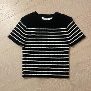 Svartvit randig ribbad topp H&M - Ribbad topp från H&M i svart och vitt med horisontella ränder. Modellen är croppad med korta ärmar och rund halsringning. Perfekt för en chill och stilren look. Materialet är stretchigt och bekvämt.