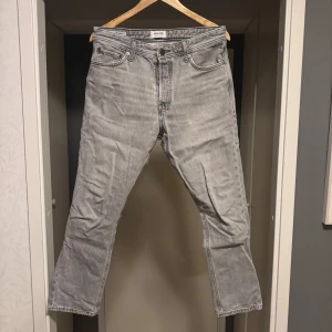 Grå jeans från Jack & Jones - Säljer ett par grå jeans från Jack & Jones med klassisk femficksdesign och raka ben. Jeansen har normal passform och är tillverkade i mjukt denimtyg. Perfekta för dig som gillar en enkel och stilren look.