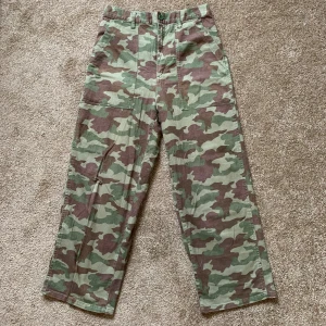 Vintage cargo byxor i camouflage  - Cargopants i grön och brun camouflage från apart by lowrys. Byxorna har raka ben, stora fickor fram och bak, samt bälteshällor. Tillverkade i bomull för en skön och avslappnad känsla. Perfekta för dig som gillar streetstyle och utility-vibe. Köpte för 10 år sedan i Japan.