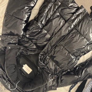 Svart pufferjacka från Calvin Klein Jeans - Säljer en svart, glansig pufferjacka från Calvin Klein Jeans. Perfekt för kalla dagar och har en riktigt snygg streetkänsla. Stor logga på insidan ger extra edge. storlek M men små i storlekne 